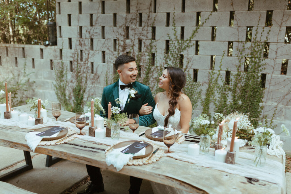 bride and groom sitting at rustic wood wedding table